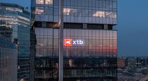 XTB corporate headquarters tower with illuminated brand signage at dusk.
