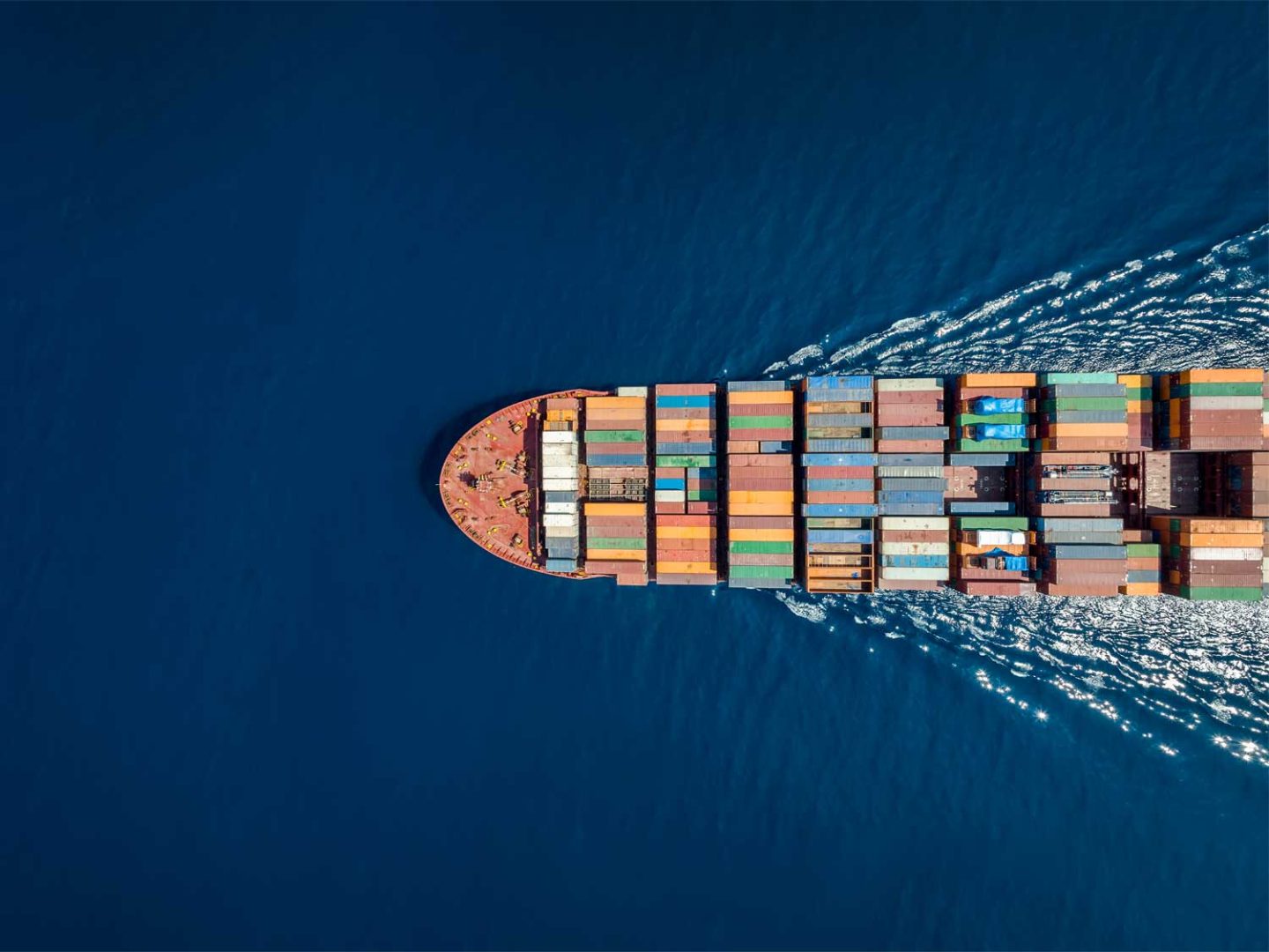 Aerial view of a container ship cutting through deep blue ocean.